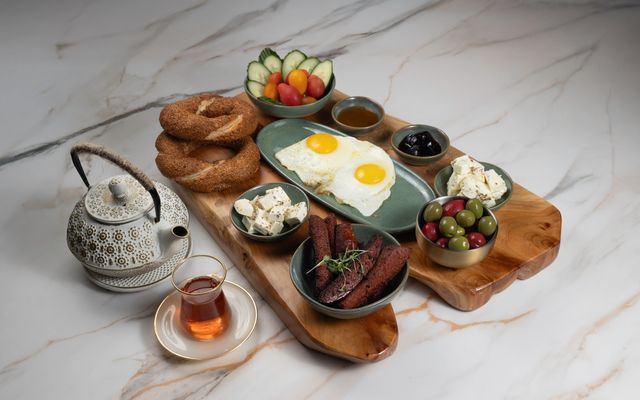 Baku Breakfast board with fried eggs, sesame bread rings, white cheese, olives, grilled sausage, cucumbers, tomatoes, honey and preserves, served with tea