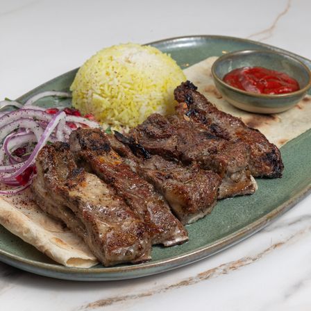 Lamb ribs kebab with rice, lavash, red onions and tomato sauce on a green plate