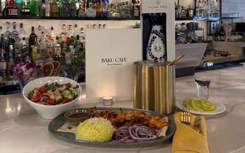Chicken kebab with saffron rice, red onion and lavash, a fresh salad and the Baku Cafe menu on the marble bar, in front of backlit shelves of bottles
