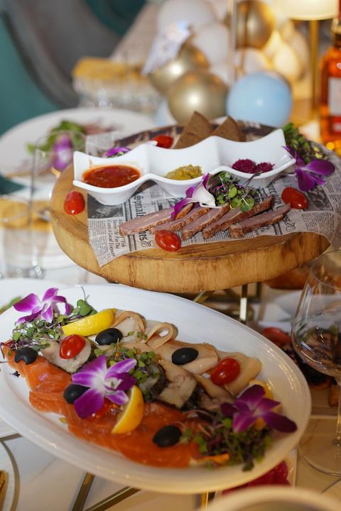 Smoked fish assortment with salmon, lemon and olives, in front of a board of sliced smoked meat with three sauces