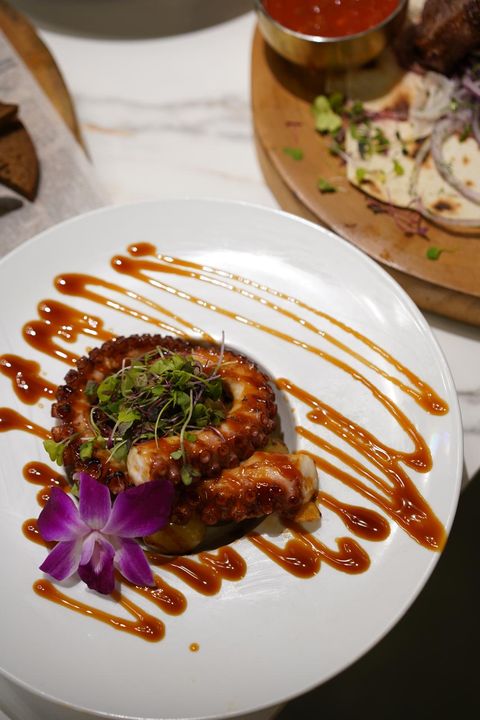 Grilled octopus over potatoes with microgreens, an orchid and a drizzled sauce