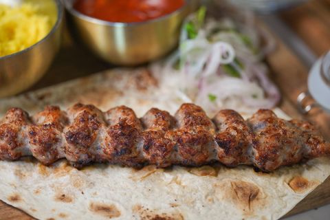 Lyulya kebab on lavash with saffron rice, red sauce and sliced onions